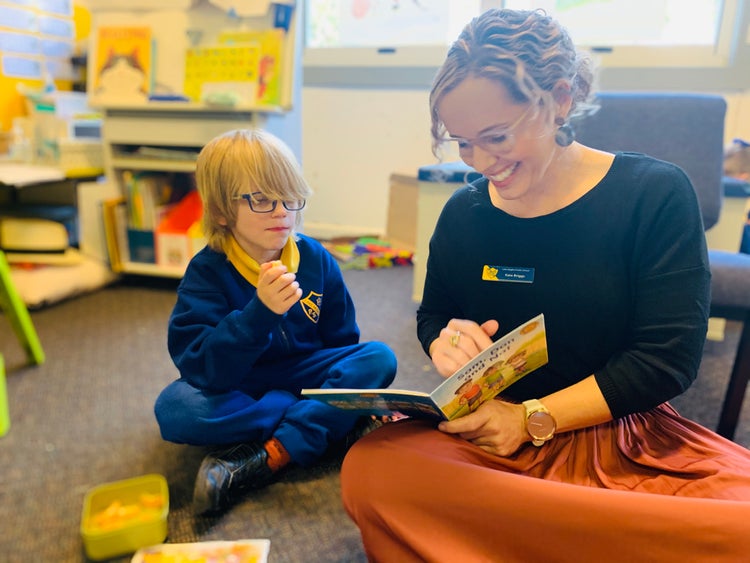 A teacher reading a book on the floor with a student