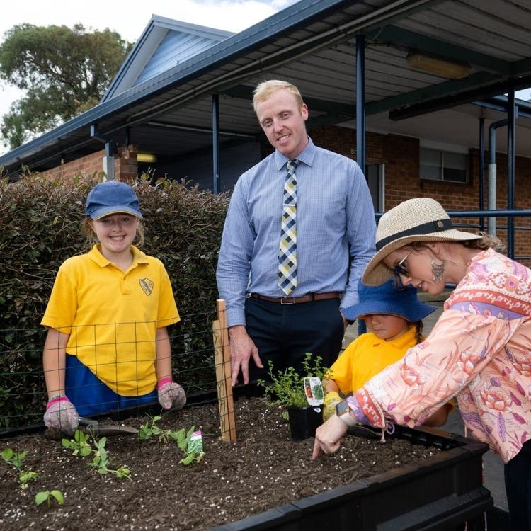 School principal standing in garden with a staff member and two students.